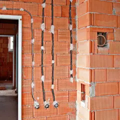 Instalacja elektryczna bezpuszkowa w trakcie budowy. Widoczne kable i otwory w ceglanych ścianach.