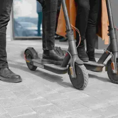 Trzy osoby stoją na chodniku obok swoich hulajnóg wyczynowych elektrycznych, gotowe do jazdy.