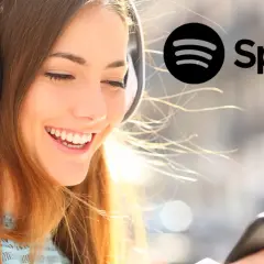 Uśmiechnięta dziewczyna w słuchawkach słucha muzyki na Spotify. Dowiedz się, jak zmienić nazwę użytkownika na Spotify.