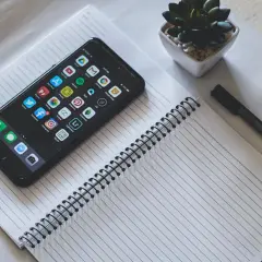 Telefon z ikonami aplikacji, w tym Facebooka, leży na notatniku. Chcesz wiedzieć, jak sprawdzić logowania na FB na telefonie?