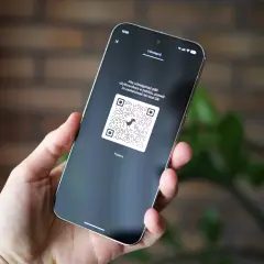 Dłoń trzyma smartfon z wyświetlonym kodem QR, który można zeskanować, aby udostępnić pliki.