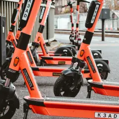 Pomarańczowe hulajnogi elektryczne trójkołowe dla dorosłych stoją w rzędzie.