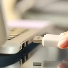 Dłoń wkłada biały pendrive do portu USB laptopa, rozpoczynając nagrywanie danych.
