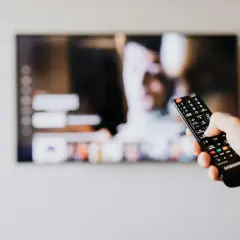 Dłoń trzyma pilot Samsunga, celując w ekran telewizora. Chcesz wiedzieć, jak wyłączyć audiodeskrypcję Samsung?