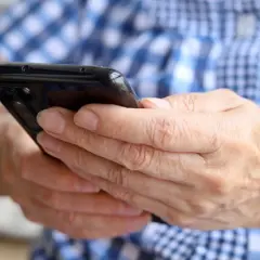 Dłonie trzymają czarny smartfon. Zastanawiasz się, jak namierzyć wyłączony telefon?