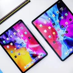 Dwa iPady z kolorową tapetą, obok linijka i niebieska okładka. Dowiedz się, jak przyspieszyć tablet.