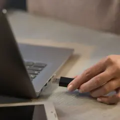 Dłoń próbuje podłączyć pendrive do laptopa, ale komputer widzi pendrive ale go nie czyta.