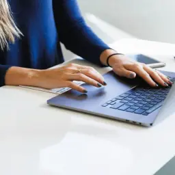 Dłonie kobiety piszącej na laptopie, czując miękki enter pod palcami.