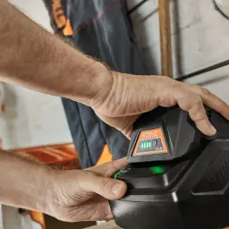 Mężczyzna wkłada akumulator Stihl do ładowarki. Zielona lampka sygnalizuje ładowanie.