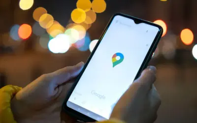 Dłoń trzyma smartfon z otwartą aplikacją Mapy Google. W tle rozmyte światła miasta. Idealne, by sprawdzić, jak znaleźć rozładowany telefon.