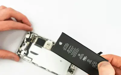 Wymiana iPhone jest potrzebna, gdy bateria jest zużyta. Dłoń trzyma nową baterię obok rozebranego telefonu.