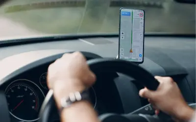 Ręce na kierownicy, przed nimi telefon z nawigacją Android pokazującą trasę i prędkość.