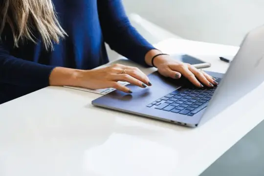 Dłonie kobiety piszącej na laptopie, czując miękki enter pod palcami.