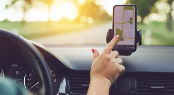 Dłoń z czerwonym lakierem na paznokciach dotyka ekranu telefonu z mapą, korzystając z nawigacji na telefon podczas jazdy.