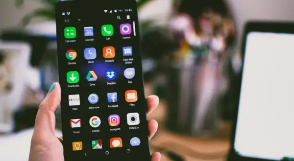 Dłoń trzyma smartfon z ikonami aplikacji. Jeśli masz problem, jak zresetować zablokowany telefon, ten ekran może pomóc.