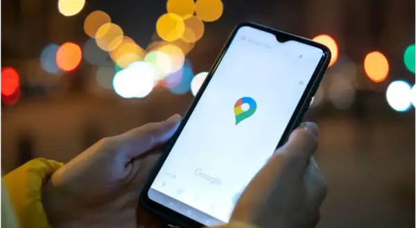 Dłoń trzyma smartfon z otwartą aplikacją Mapy Google. W tle rozmyte światła miasta. Idealne, by sprawdzić, jak znaleźć rozładowany telefon.