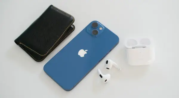 Niebieski iPhone 13, który wyszedł we wrześniu 2021, leży obok czarnego etui i białych słuchawek AirPods.