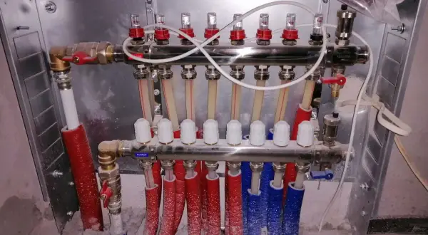 System ogrzewania podłogowego z rozdzielaczem. Widać tu miedziane rurki i zawory, a także biały, wielożyłowy kabel do termostatu pokojowego.