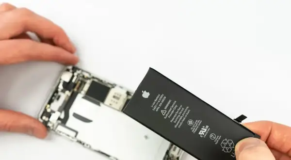 Wymiana iPhone jest potrzebna, gdy bateria jest zużyta. Dłoń trzyma nową baterię obok rozebranego telefonu.