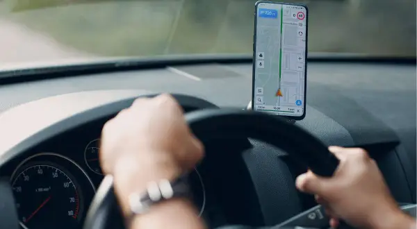 Ręce na kierownicy, przed nimi telefon z nawigacją Android pokazującą trasę i prędkość.