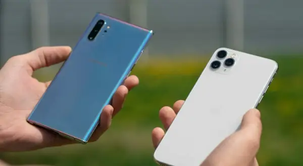 Dwie dłonie trzymają telefony: niebieski Samsung i biały iPhone. Który wybierasz?