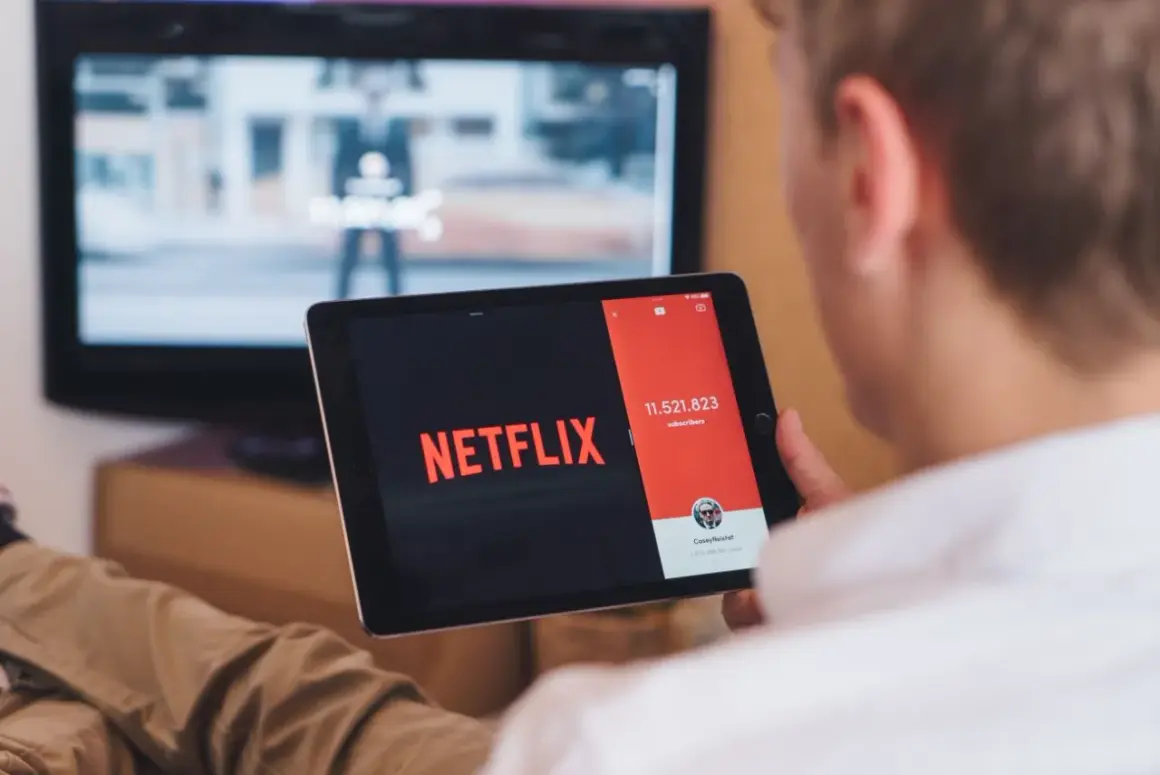 Chcesz wiedzieć, jak podłączyć tablet do telewizora przez HDMI? Na ekranie tabletu widać logo Netflix, a w tle telewizor.