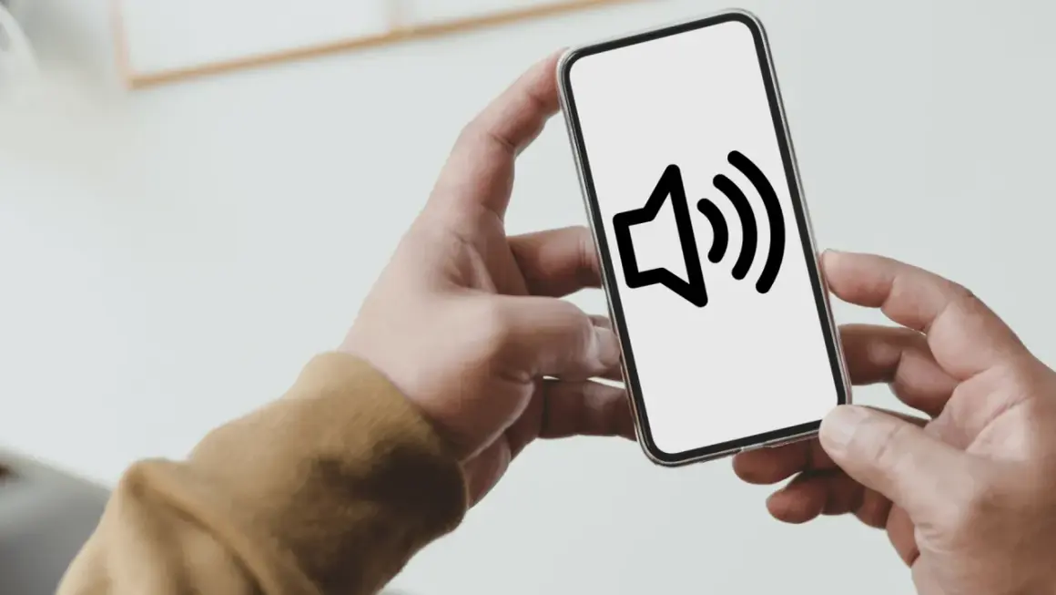 Dłoń trzyma smartfon z ikoną głośnika. Dowiedz się, jak wyłączyć dźwięk klawiszy Samsung, by pisać ciszej.