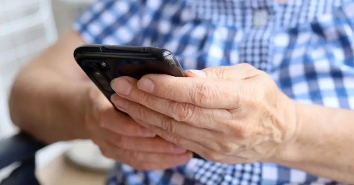Dłonie trzymają czarny smartfon. Zastanawiasz się, jak namierzyć wyłączony telefon?