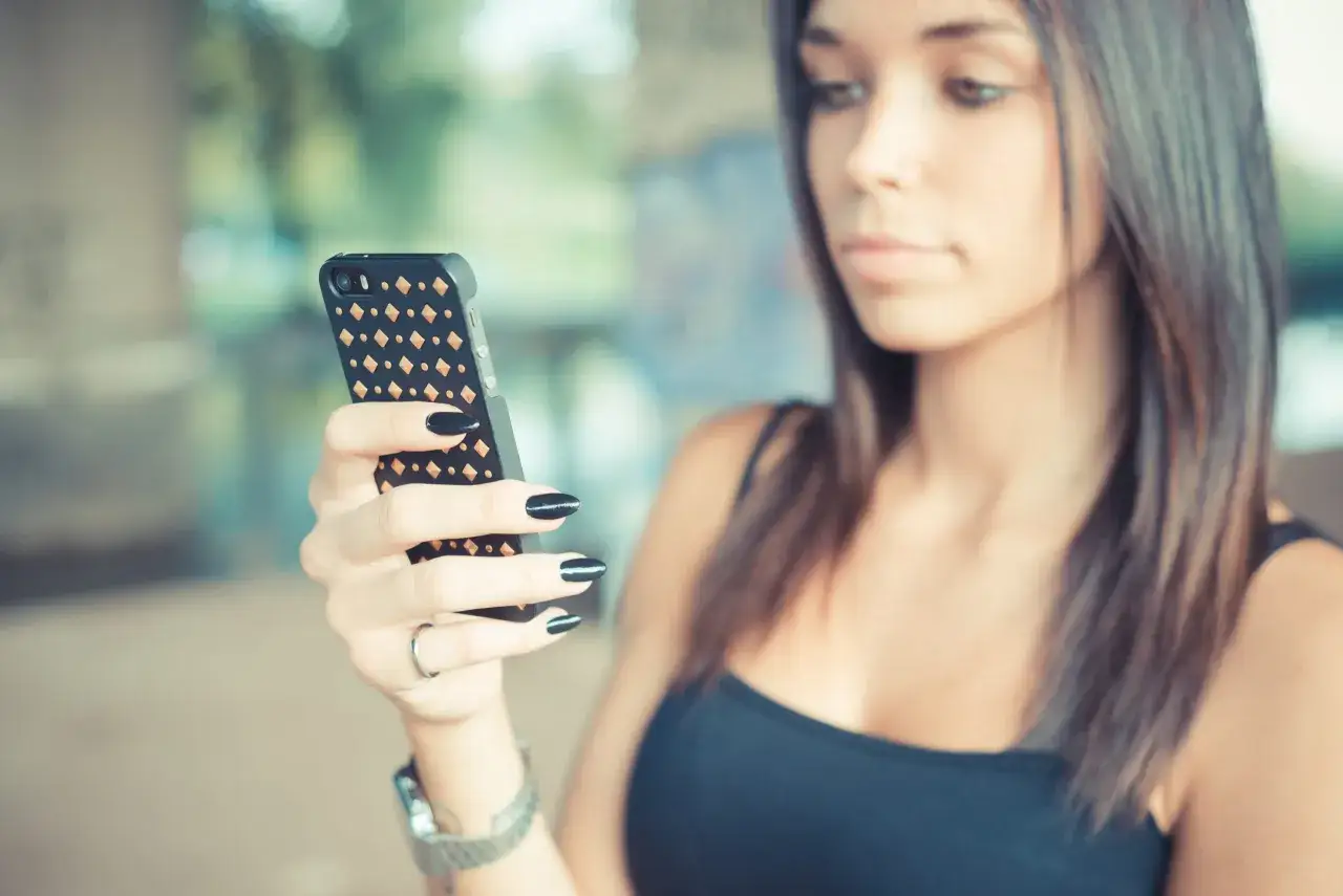 Kobieta z czarnym lakierem na paznokciach trzyma telefon, szukając informacji, jak usunąć konto na Badoo w telefonie.