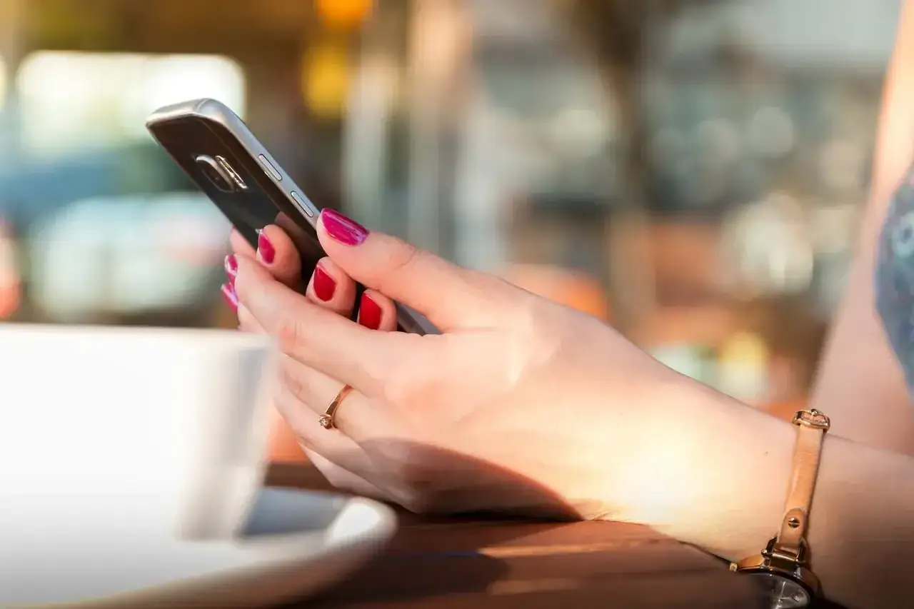 Kobieta z czerwonymi paznokciami trzyma telefon, szukając informacji, jak wyłączyć pocztę głosową Orange.