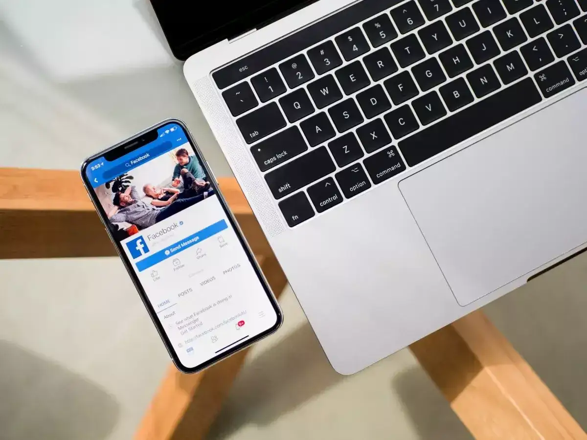 Telefon z Facebookiem obok laptopa. Chcesz wiedzieć, jak wylogować FB ze wszystkich urządzeń?
