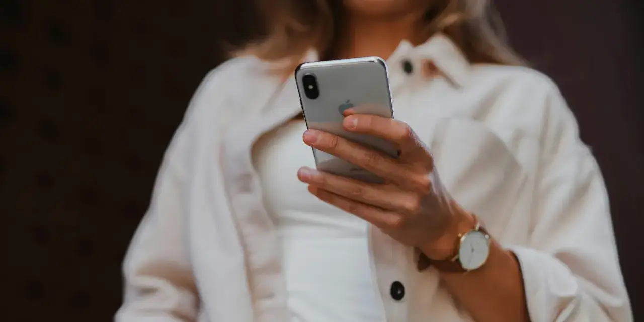 Kobieta trzyma iPhone'a, być może szukając informacji, jak sprawdzić historię telefonu.
