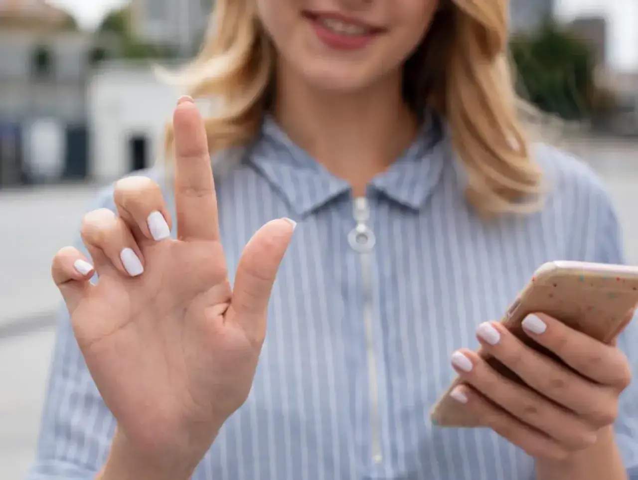 Kobieta z białymi paznokciami trzyma telefon, jakby szukała sposobu, jak namierzyć wyłączony telefon.