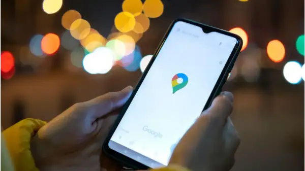 Dłoń trzyma smartfon z otwartą aplikacją Mapy Google. W tle rozmyte światła miasta. Idealne, by sprawdzić, jak znaleźć rozładowany telefon.