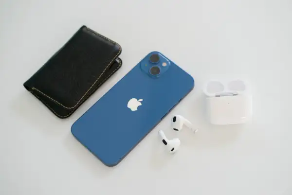 Niebieski iPhone 13, który wyszedł we wrześniu 2021, leży obok czarnego etui i białych słuchawek AirPods.