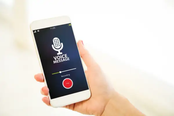 Dłoń trzyma smartfon z włączonym dyktafonem w telefonie. Na ekranie widnieje ikona mikrofonu i napis "Voice Message".