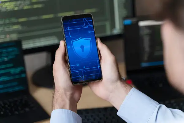 Ręce trzymają smartfon z ikoną tarczy i klucza, symbolizującą rozwiązanie problemu, jak odblokowac telefon Samsung gdy zapomni sie kodu.