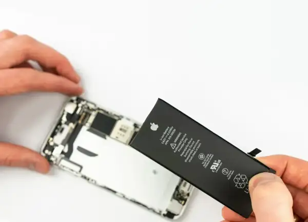 Wymiana iPhone jest potrzebna, gdy bateria jest zużyta. Dłoń trzyma nową baterię obok rozebranego telefonu.