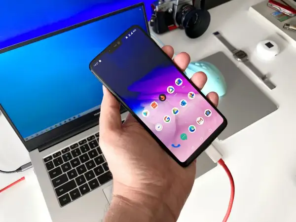 Podłączony do laptopa smartfon, gotowy do transferu danych. Prosty sposób, jak zgrać zdjęcia z telefonu na komputer.